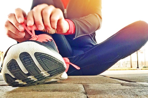 Woman sitting on the ground tying her running shoe