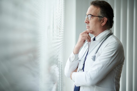 Pensive head of medical clinic rubbing chin and looking through office window