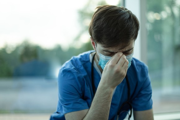 Man in medical scrubs with head down looking tired.