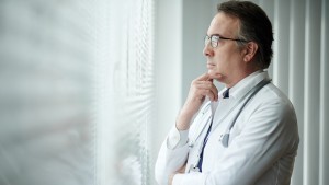 Pensive head of medical clinic rubbing chin and looking through office window