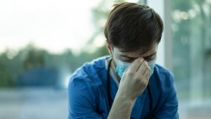Man in medical scrubs with head down looking tired
